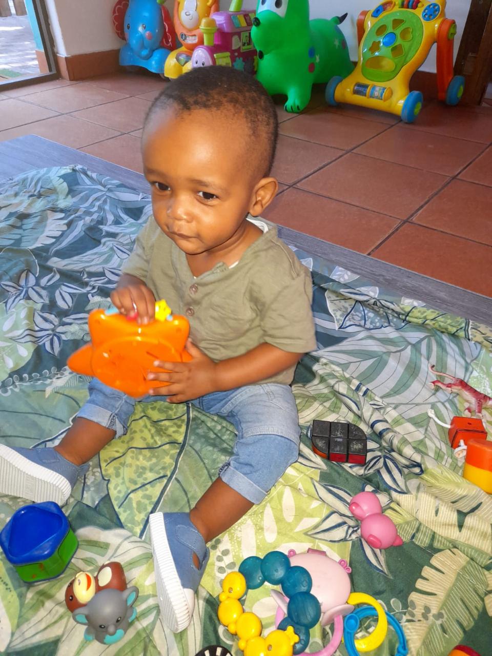 A baby sitting on a soft play mat exploring colourful toys in the baby room