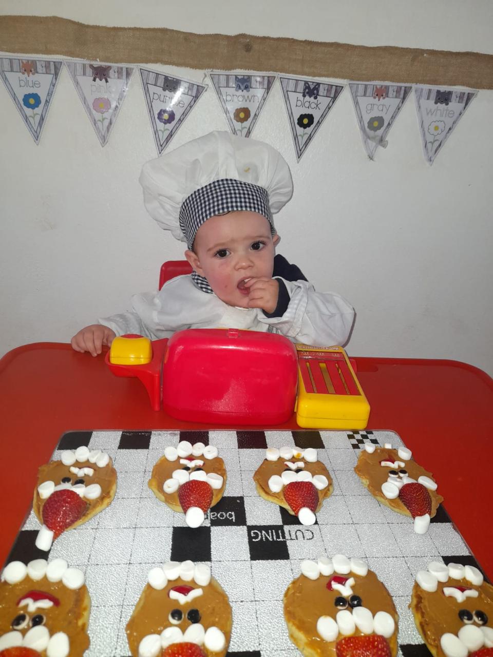 A baby in a chef's hat at the cooking table with decorated pancake faces