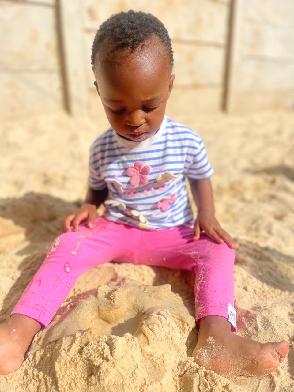 A toddler sitting in the sandpit, quietly exploring the warm sand
