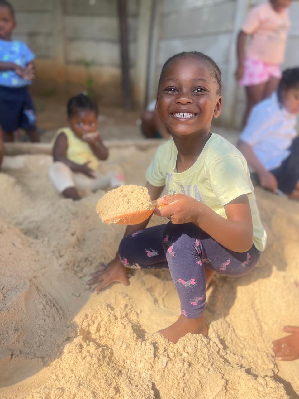 A happy girl scooping sand with a spade in the sandpit