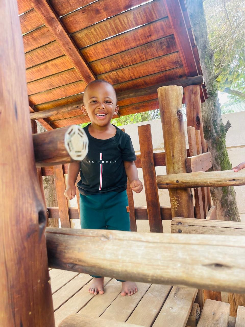 A laughing boy playing inside the wooden treehouse on the playground